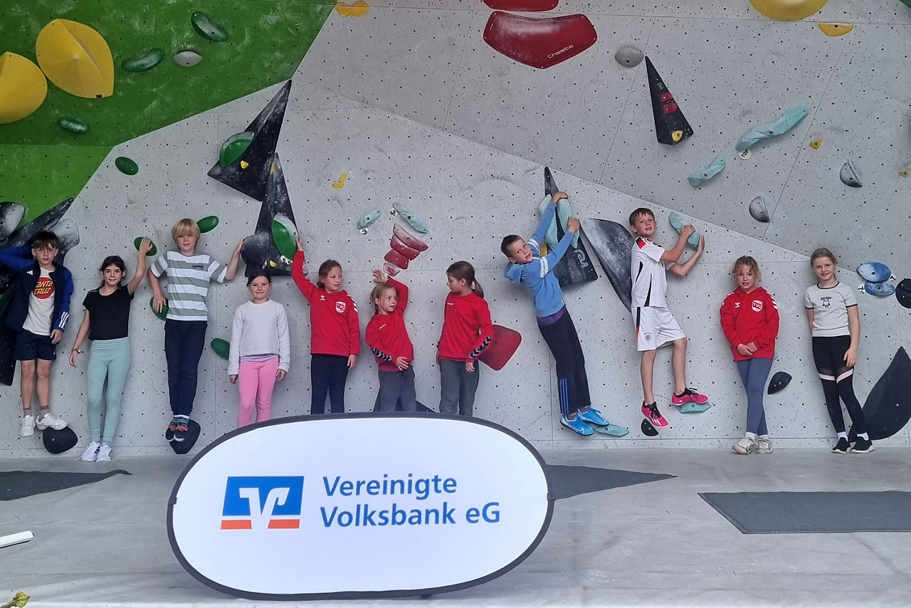 Elf Kinder an einer Boulderwand, davor ein Aufsteller der Vereinigten Volksbank eG