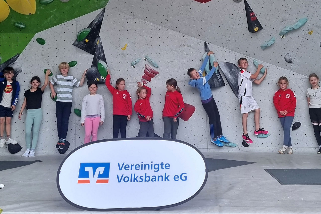 Elf Kinder an einer Boulderwand, davor ein Aufsteller der Vereinigten Volksbank eG