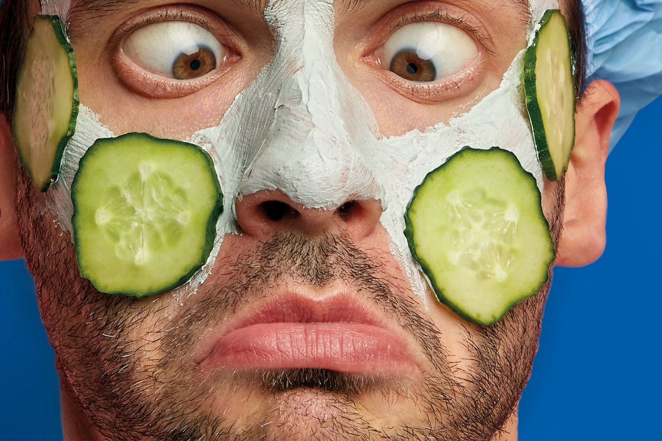 Ein Mann mit einer Gesichtsmaske und Gurkenscheiben im Gesicht schielt auf seine Nase