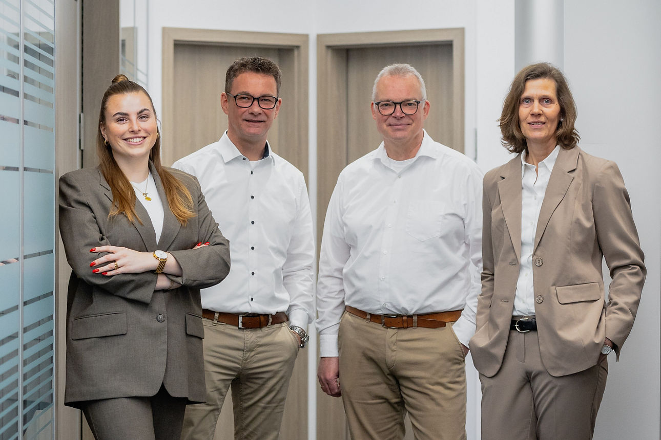 Eine Gruppe von vier Geschäftsleuten, die gemeinsam in einem modernen Büroflur posieren.