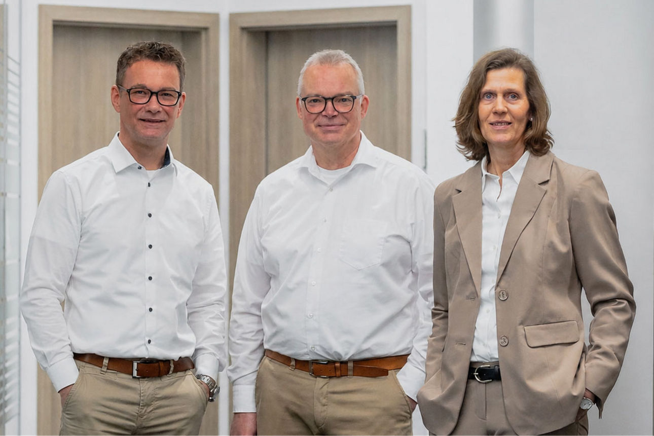 Eine Gruppe von drei Geschäftsleuten, die gemeinsam in einem modernen Büroflur posieren.