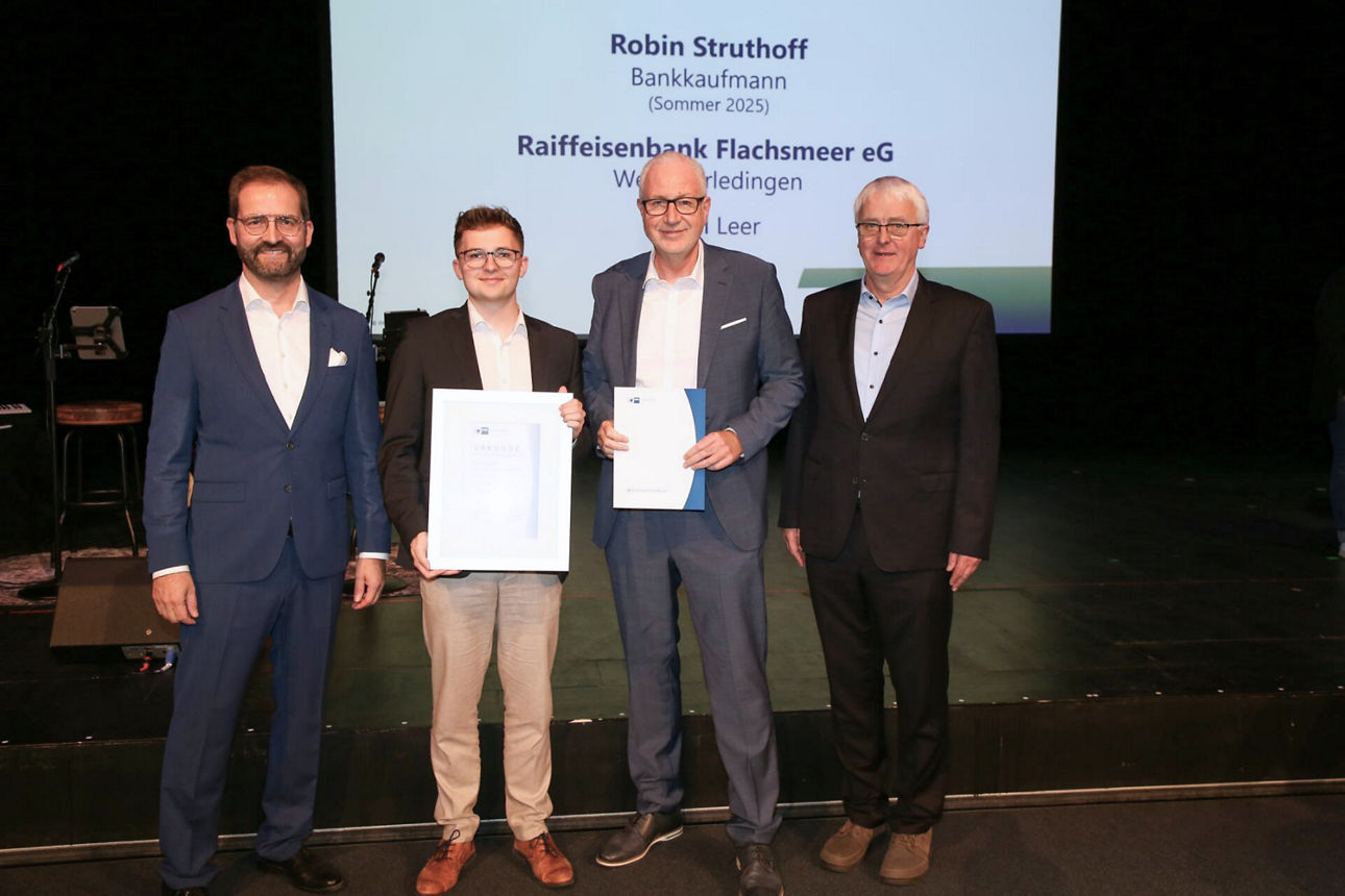 Ein junger Mann hält stolz ein gerahmtes Zertifikat neben seinen Kollegen während einer Ehrungsveranstaltung auf der Bühne.