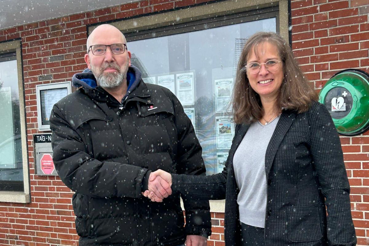 Zwei Personen geben sich vor einem Backsteingebäude bei leichtem Schneefall im Freien die Hand.