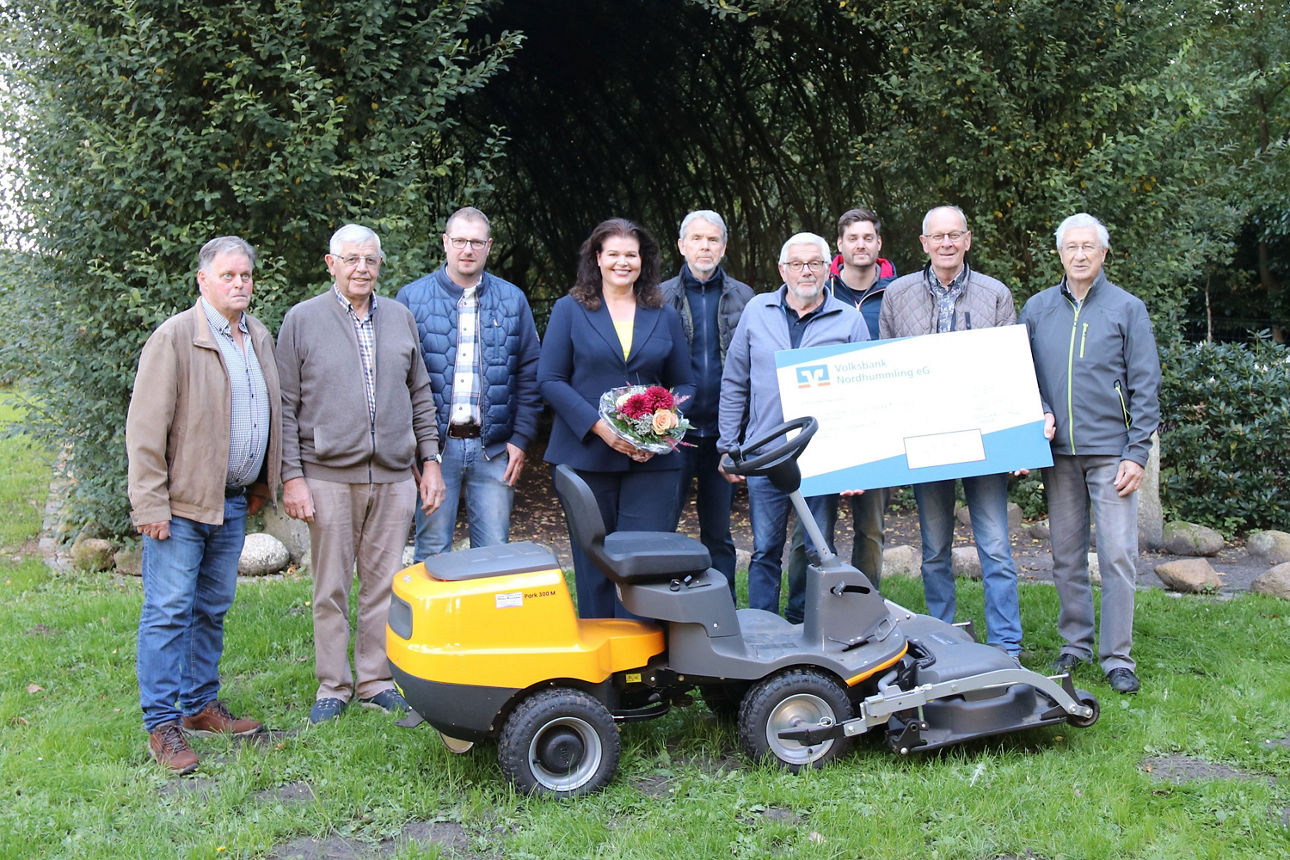 Gruppe von neun Personen vor einem Aufsitzmäher, die einen Spendenscheck halten