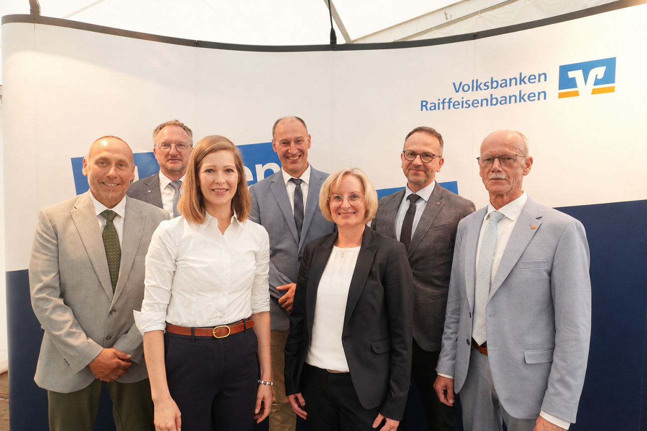 Eine Gruppe von Menschen, die gemeinsam vor einer Kulisse mit dem Logo der Volksbanken und Raiffeisenbanken stehen.