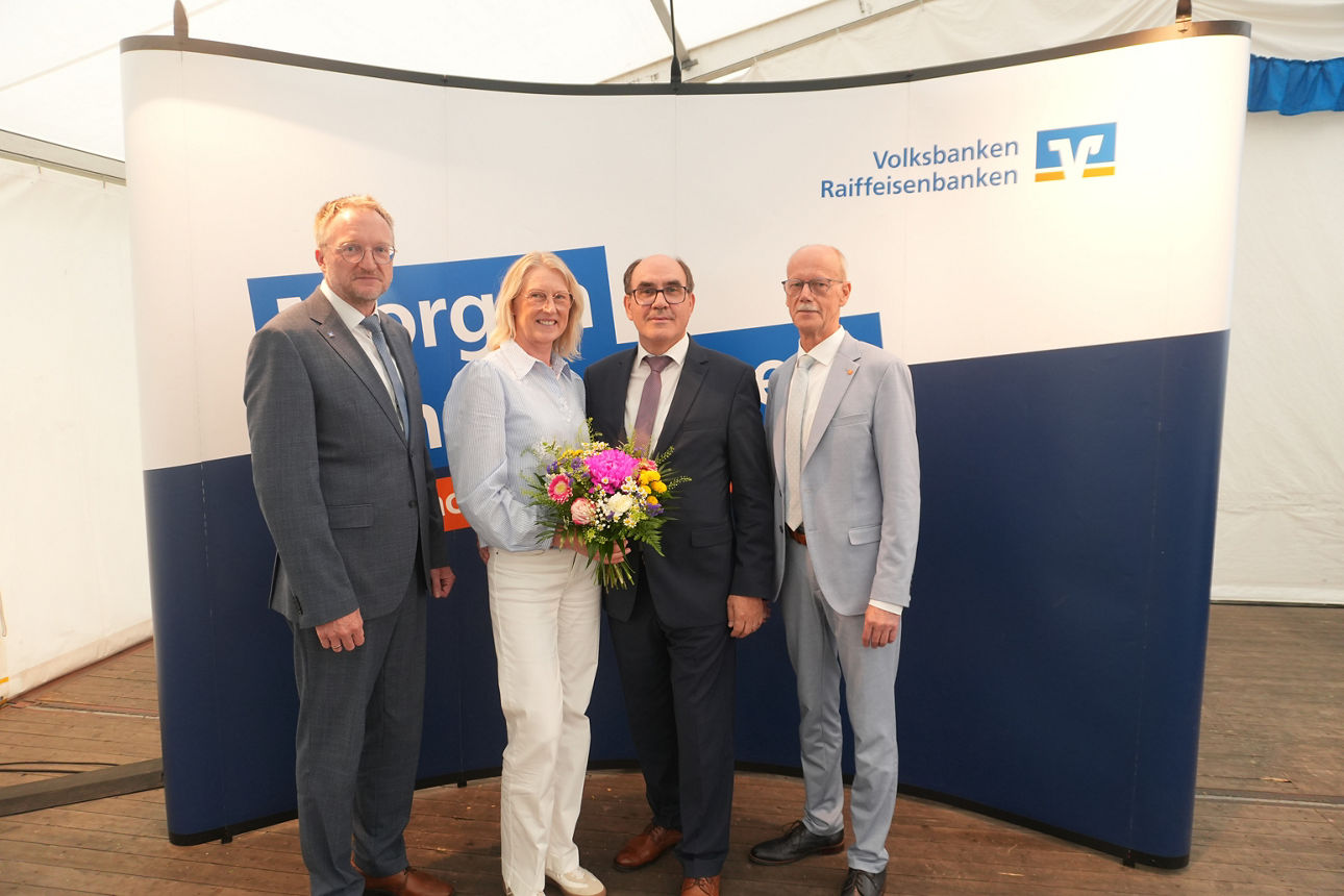 Eine Gruppe von vier Personen, die gemeinsam vor einer Kulisse mit dem Logo der Volksbanken Raiffeisenbanken stehen.