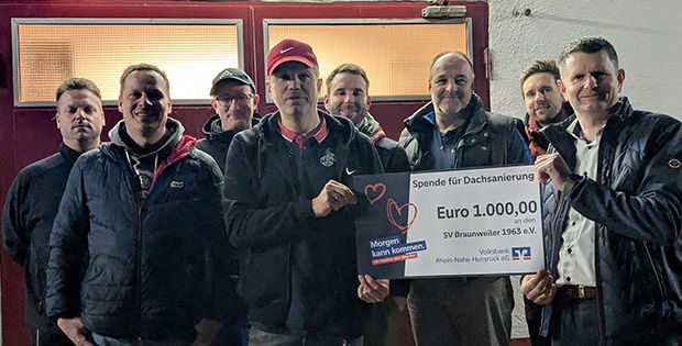 Eine Gruppe von Menschen, zwei Personen im Vordergrund halten einen Spendenscheck in den Händen.
