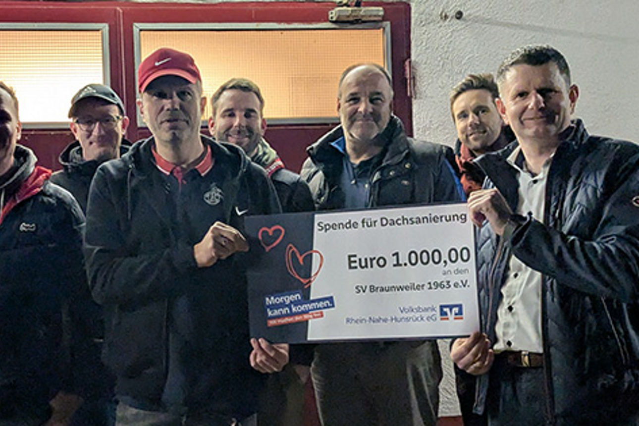 Eine Gruppe von Menschen, zwei Personen im Vordergrund halten einen Spendenscheck in den Händen.
