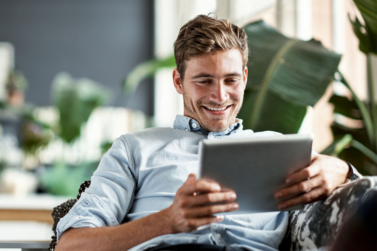 Shot of a happy young man using his tablet while relaxing on the couch at home