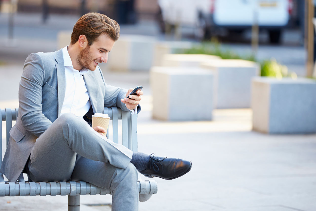 Ein Mann sitzt auf einer Bank mit einem Smartphone in der Hand