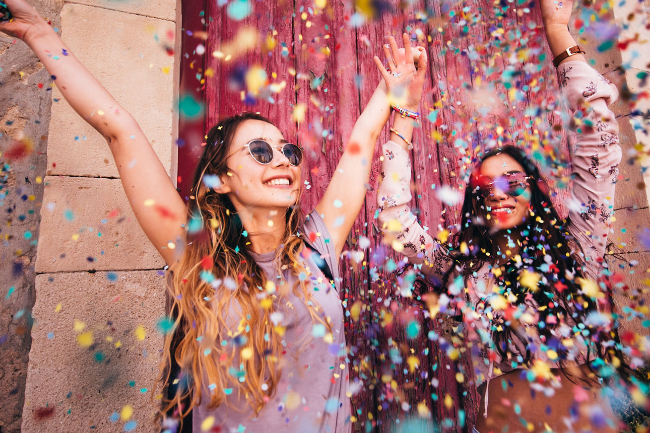 Cheerful multi-ethnic female teenage best friends partying by throwing confetti in city streets