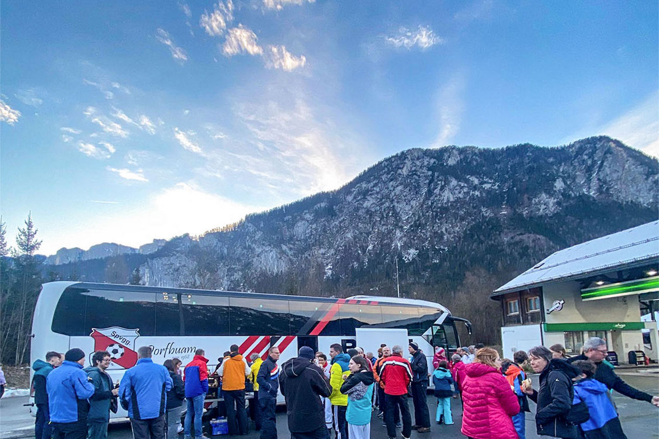 Ein Skigebiet in den Bergen. Davor steht ein Bus mit vielen Personen.