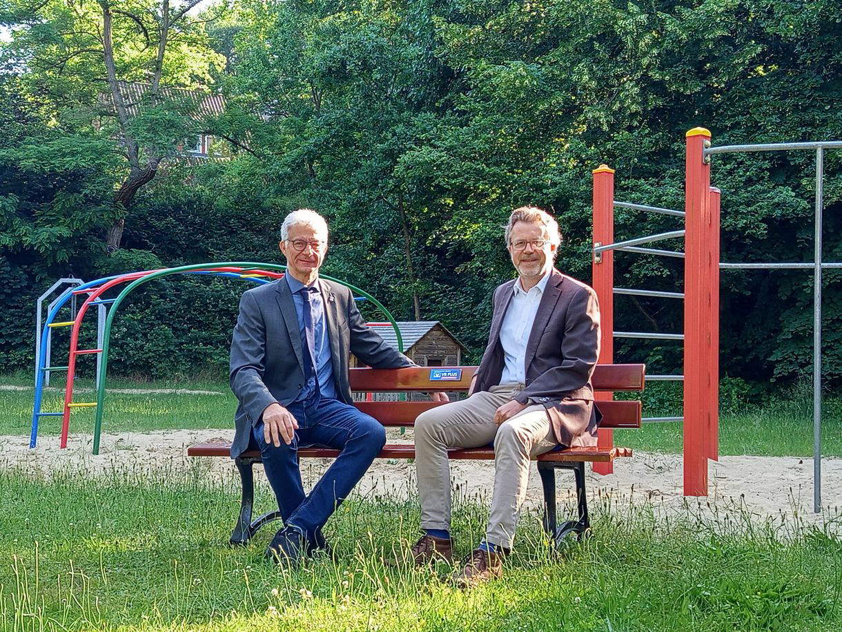 Zwei Herren sitzen auf der gespendeten Bank auf einer Wiese. 