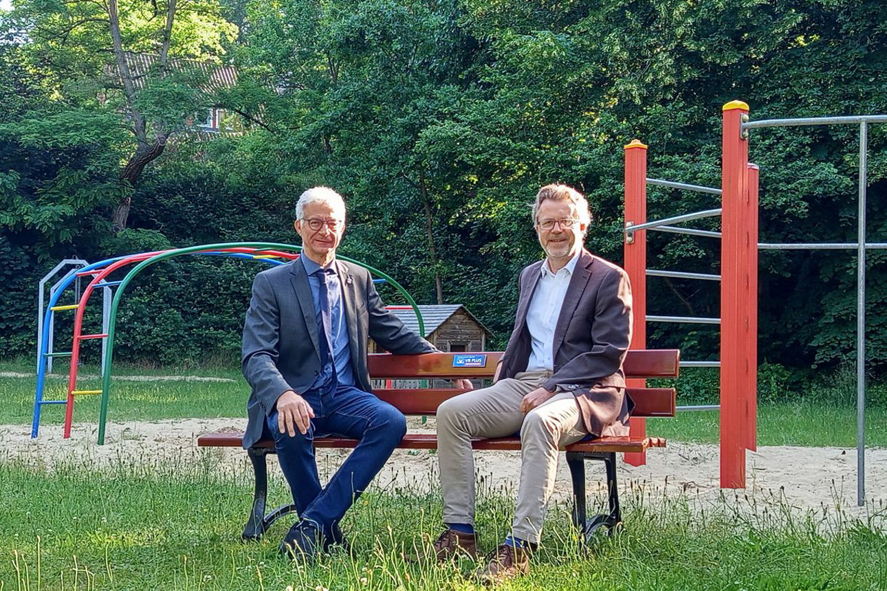 Zwei Herren sitzen auf der gespendeten Bank auf einer Wiese. 
