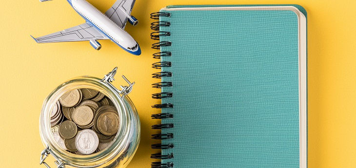 Glas mit Muenzen neben Notizblock und symbolisch verwendetem Modellflugzeug