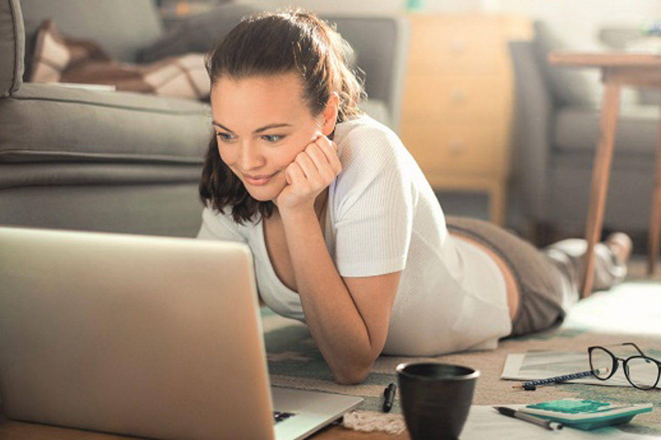Frau arbeitet auf dem Boden liegend am Laptop