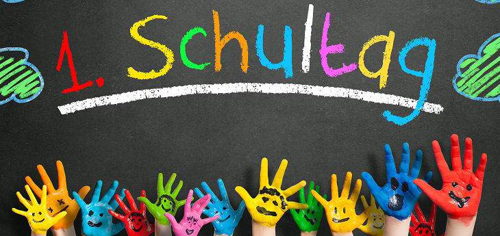 Bunte Kinderhände vor Tafel mit Aufschrift 1. Schultag