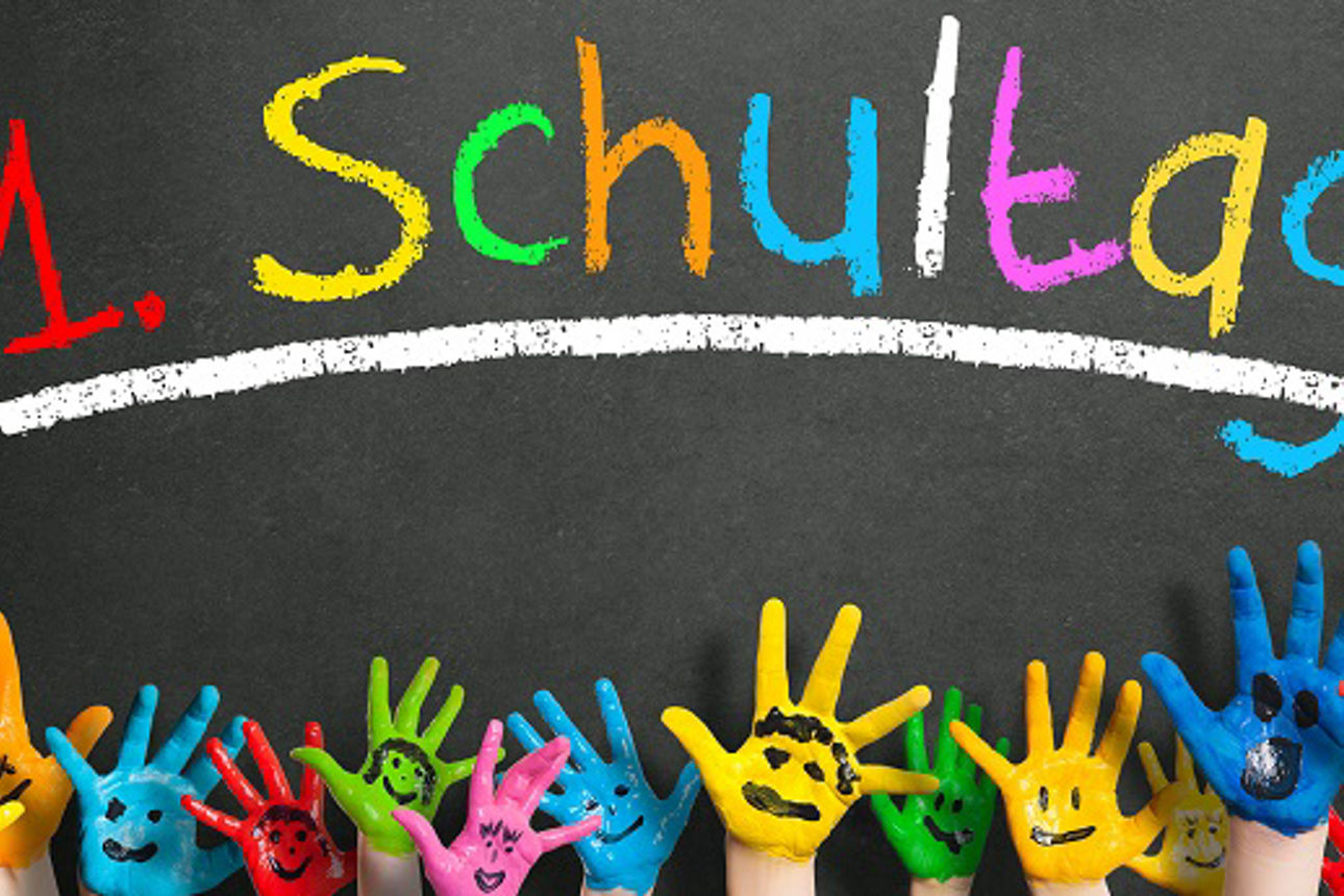 Bunt bemalte Kinderhände vor Tafel mit Aufschrift 1. Schultag