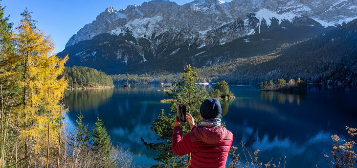 Herbstlandschaft mit Gebirge und Rückenansicht fotografierender Person im Vordergrund