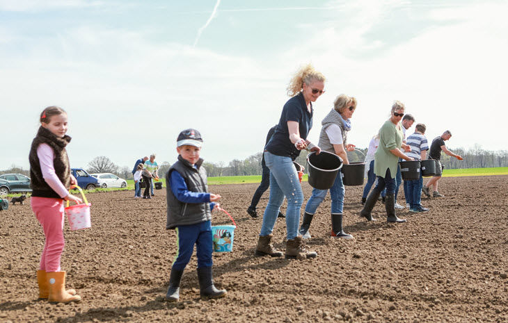 Mehrere Erwachsene und Kinden streuen auf einem Feld Saatgut.