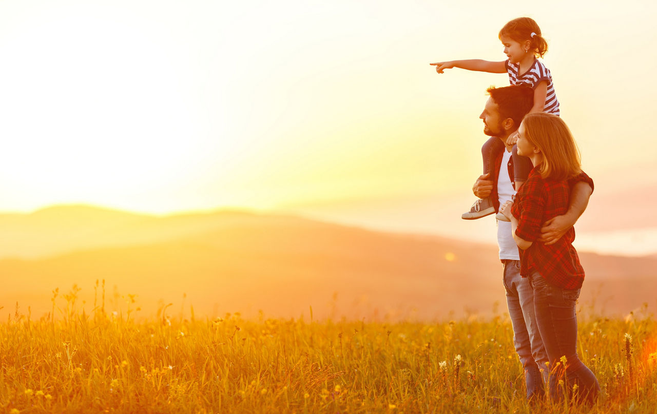 Vater, Mutter und Kind schauen in den Sonnenuntergang