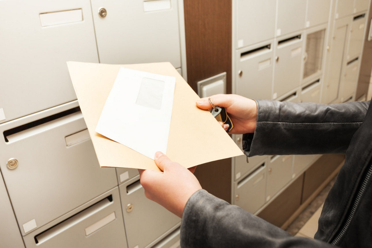 Eine Person hält Briefe vor einem Briefkasten