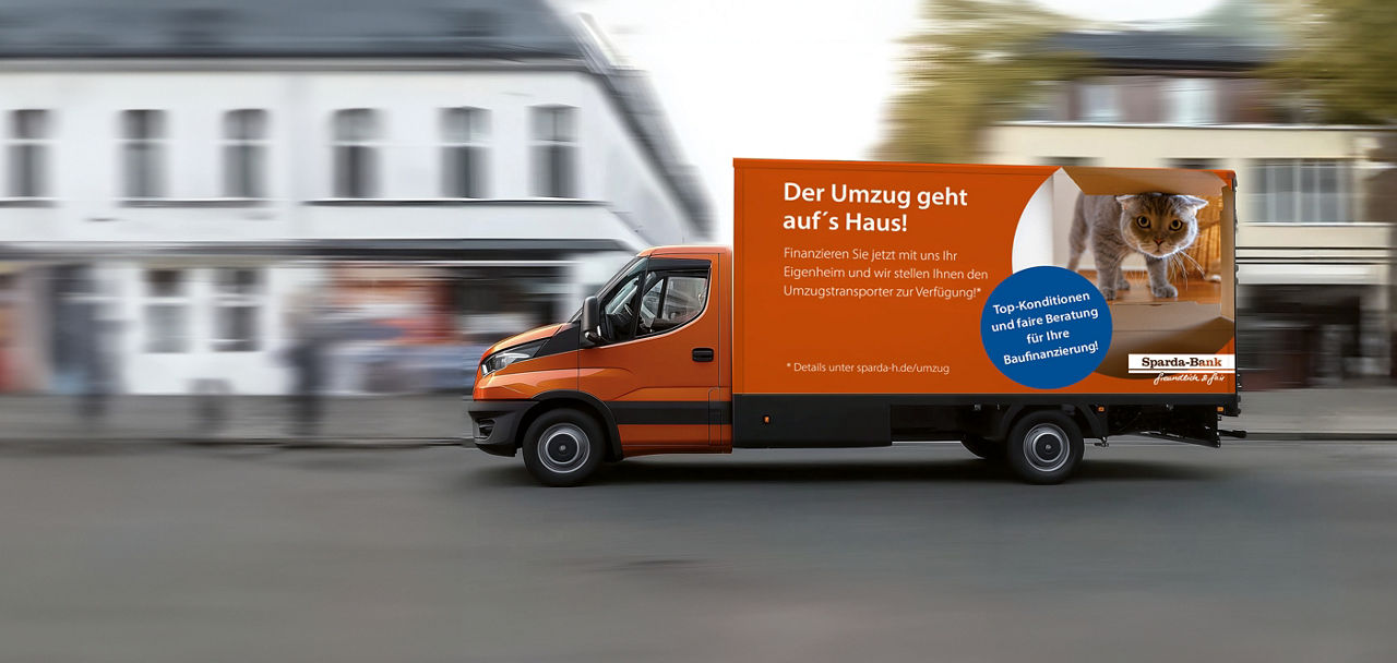 Auf einer Strasse vor zwei Gebäuden fährt ein Transporter mit Werbung der Sparda-Bank Hannover