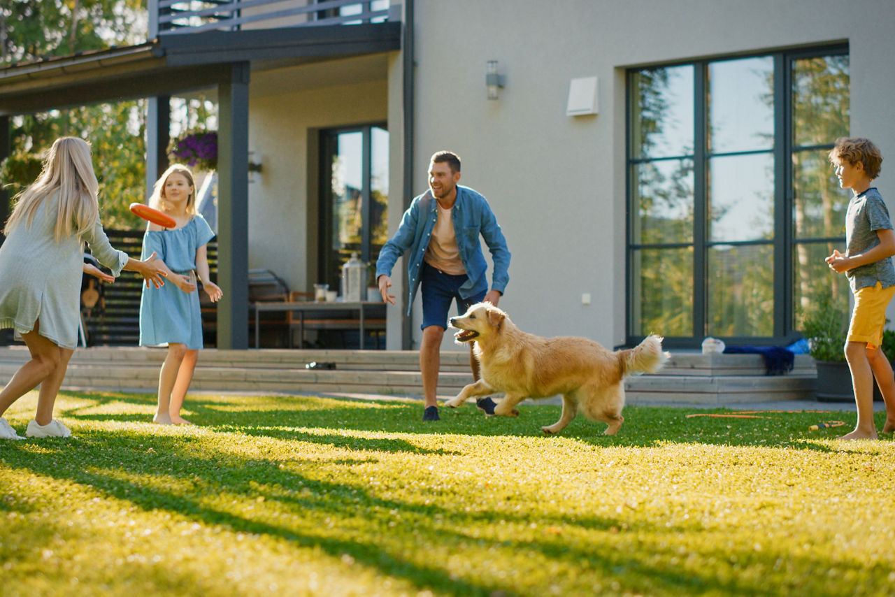 Eine vierköpfige Familie spielt mit einem Hund auf dem Rasen vor einem Haus