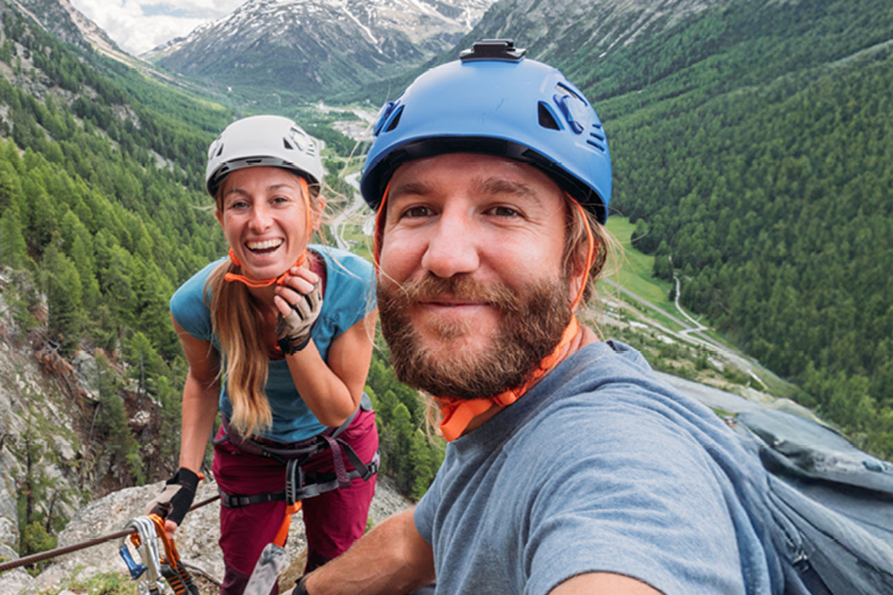 Zwei Menschen in Kletterkleidung auf einem Berg lächeln in die Kamera