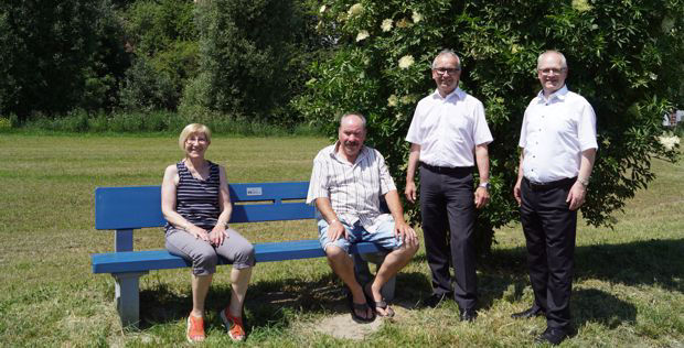 Vier Personen stehen und sitzen auf einer blauen Bank auf einer Wiese.