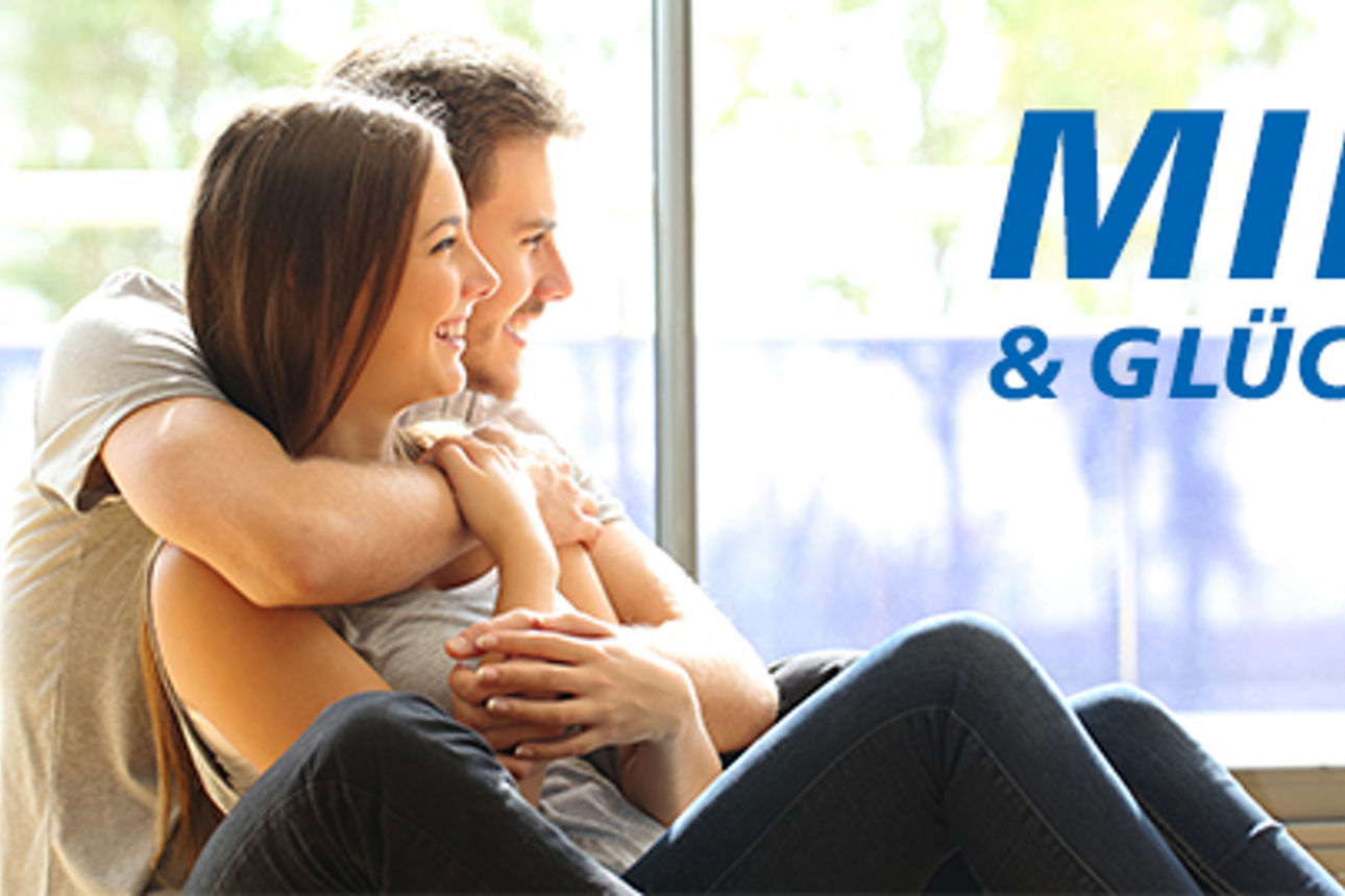 Ein junges Paar sitzt am Fenster, der Mann hat den Arm um die Frau gelegt