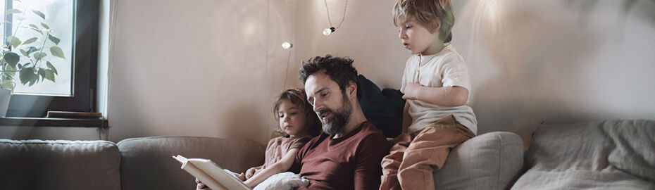 Ein Vater liest seinen zwei Kindern etwas auf der Couch vor