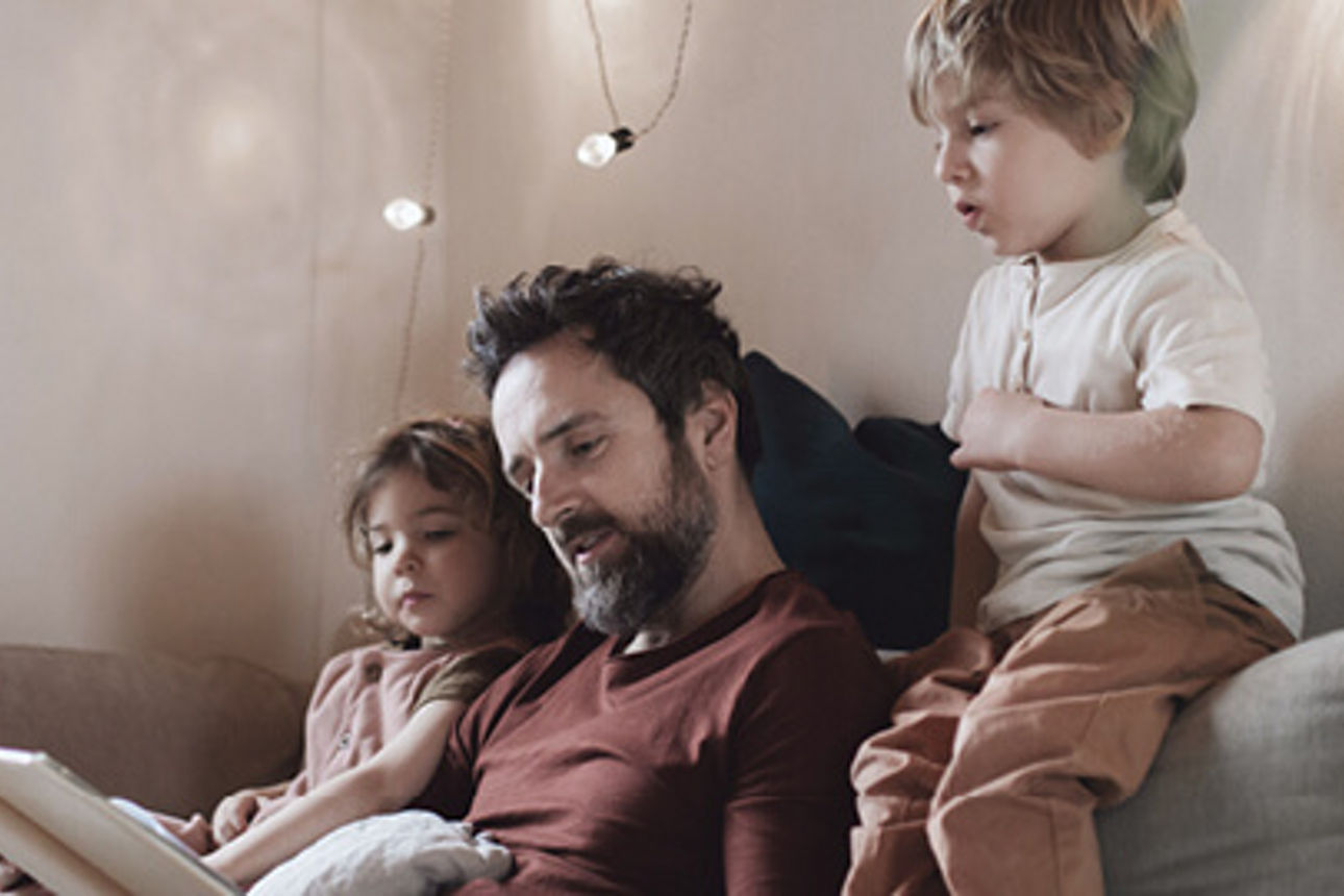 Ein Vater liest seinen zwei Kindern etwas auf der Couch vor