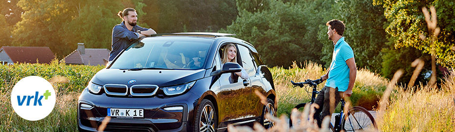Eine Frau in einem E-Auto und zwei Männer unterhalten sich