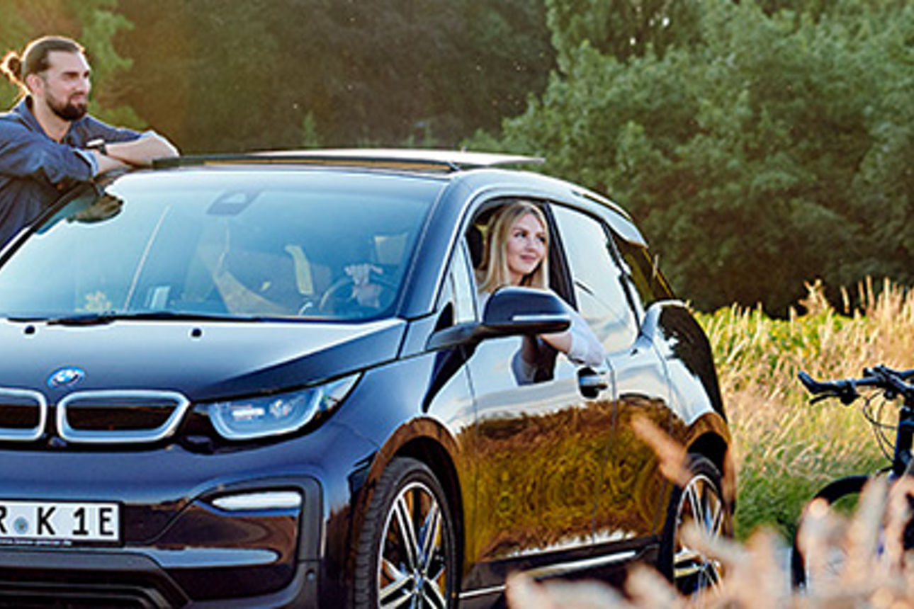 Eine Frau in einem E-Auto und zwei Männer unterhalten sich