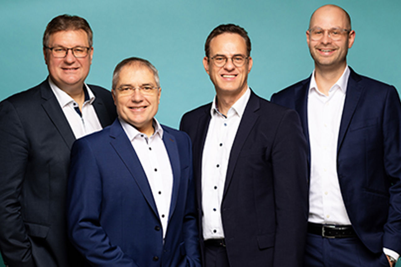 4 Vorstände im Anzug vor einfarbigen Hintergrund