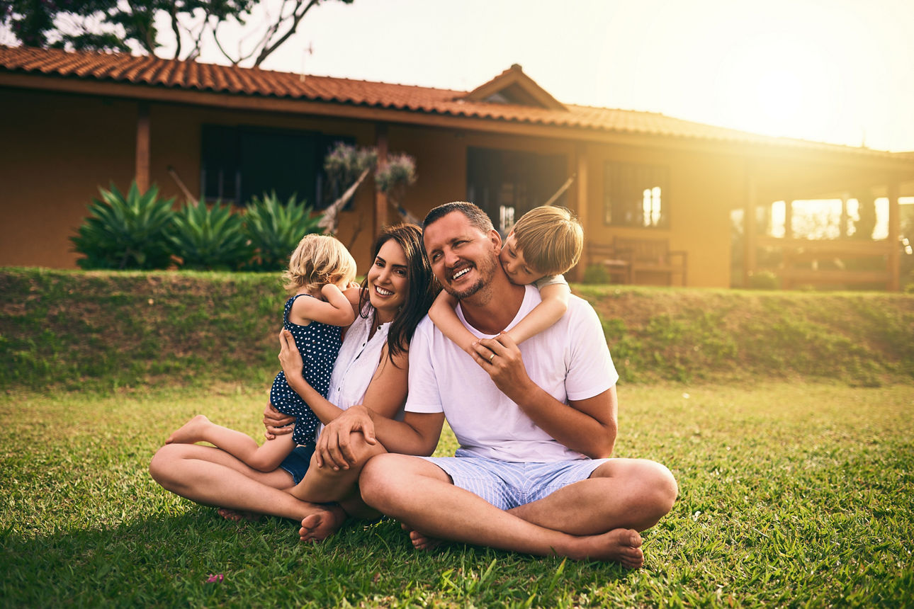 Vierköpfige Familie sitzt glücklich vor ihrem Haus.