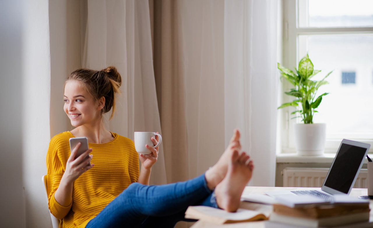 Frau mit gelben Shirt und Handy in der Hand am Kaffee trinken