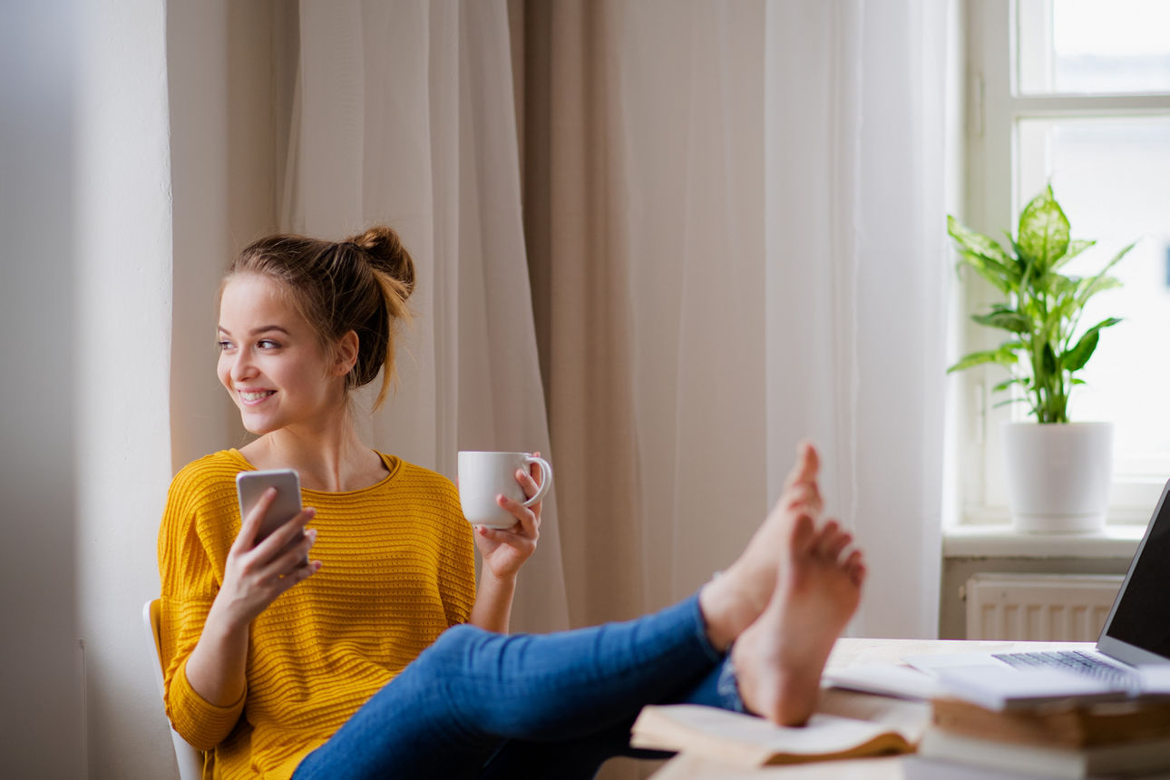 Frau mit gelben Shirt und Handy in der Hand am Kaffee trinken