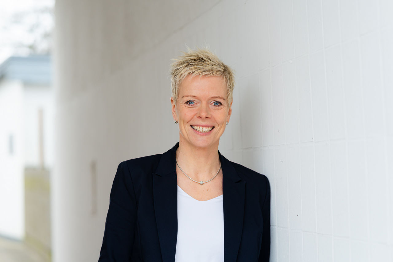 Eine lächelnde Frau mit kurzen Haaren vor einer weißen Wand