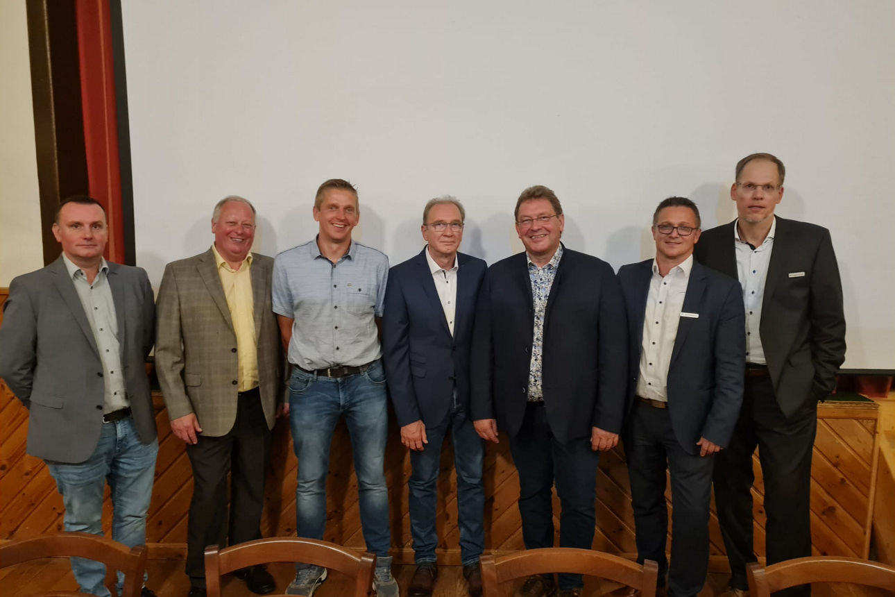 Sieben Männer in einer Reihe vor einer weißen Bühne