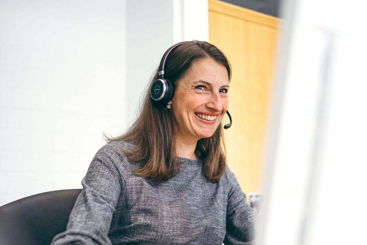 Sympathische Frau sitzt mit Headset lächelnd am PC in einem Beratungsgespräch