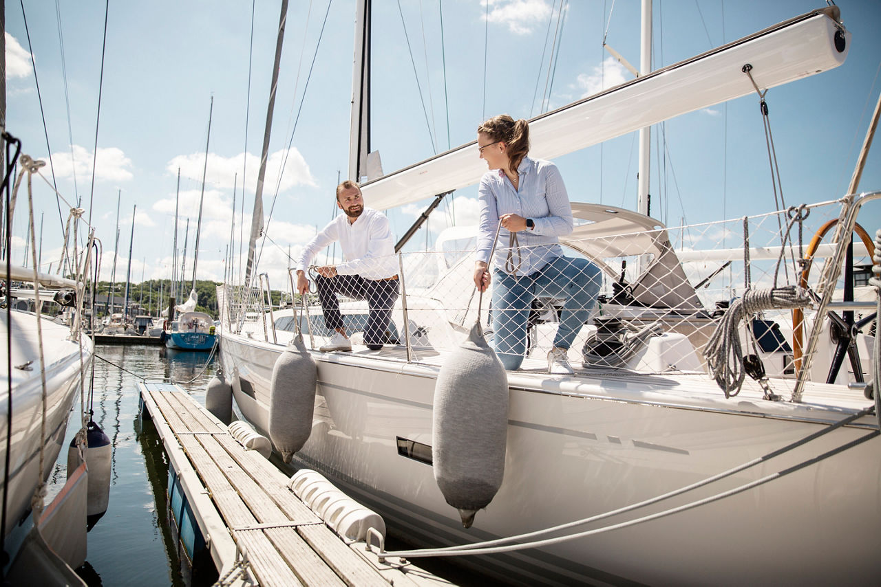 Zwei Menschen lachen sich bei  Sonnenschein an, während sie gemeinsam an Deck einer Segelyacht arbeiten 