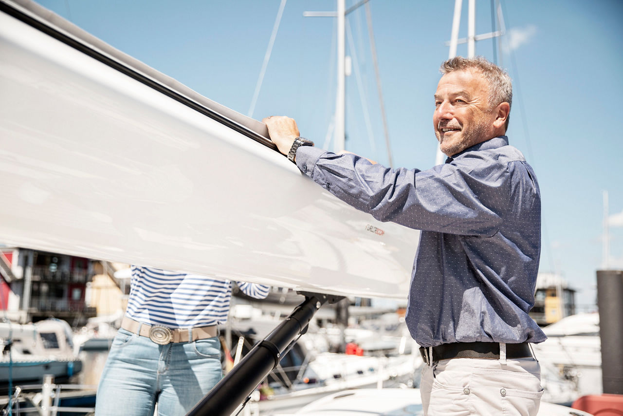 Ein Mann steht auf einem Segelboot und richtet das Segel aus.