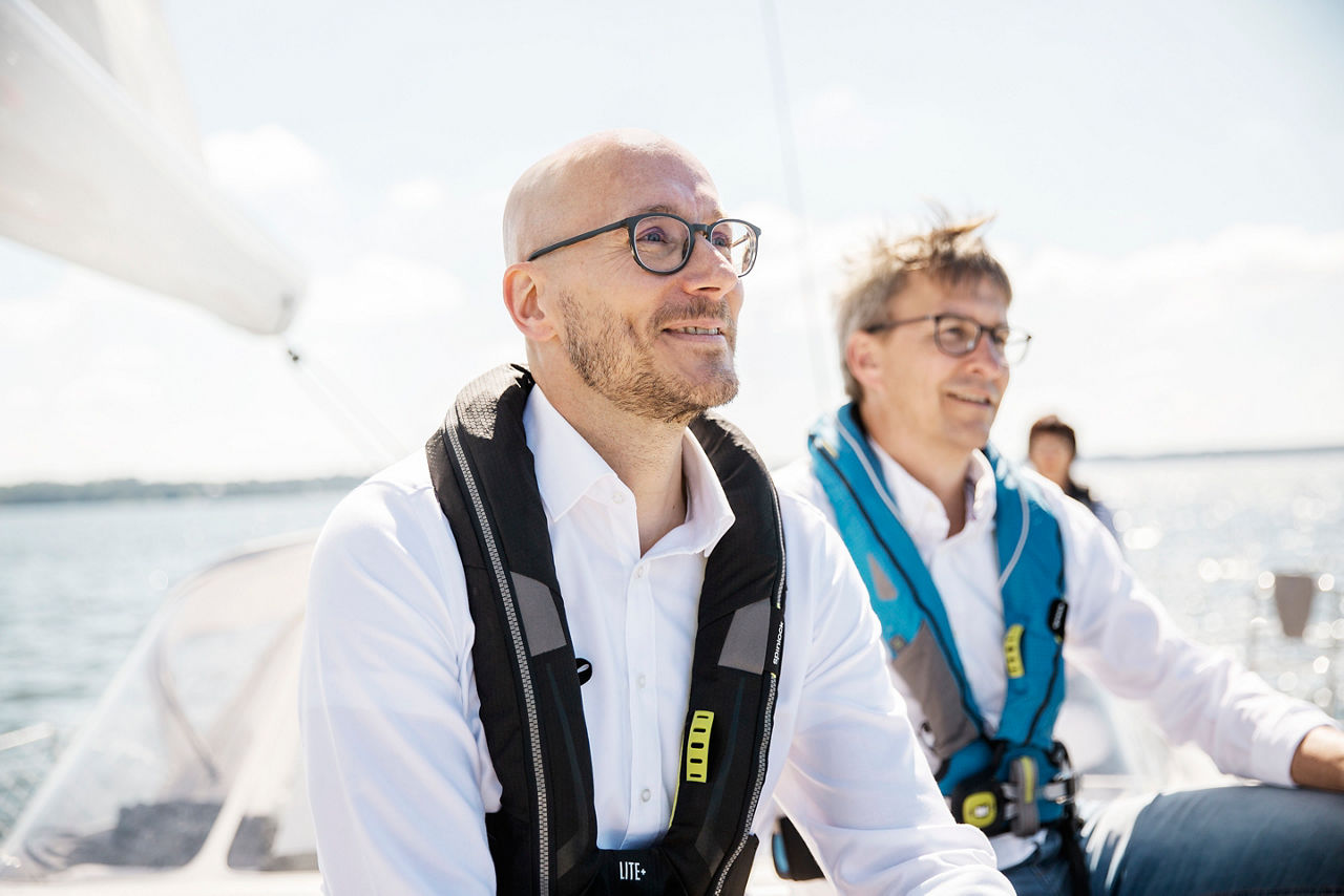 Zwei Männer sitzen beide auf einem Segelboot und schauen in den Horizont.