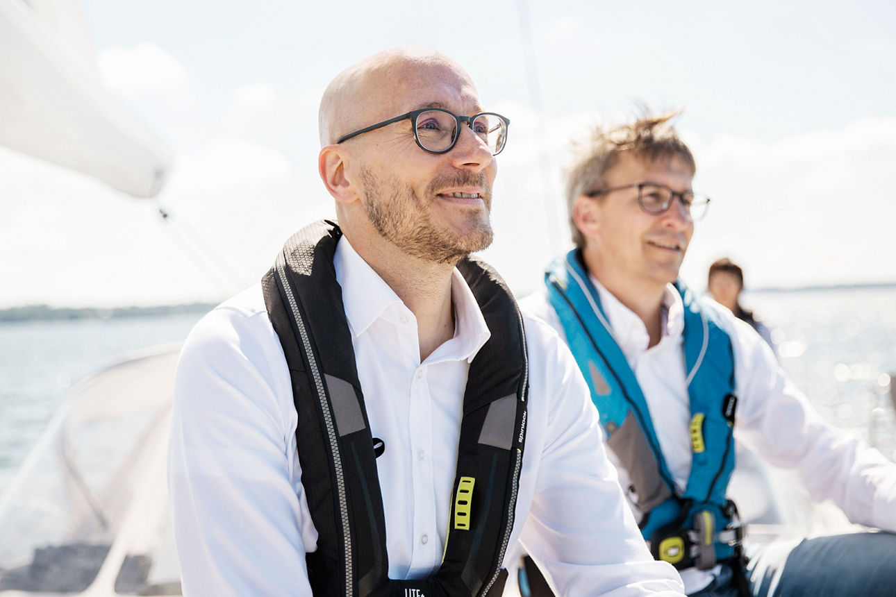 Zwei Männer sitzen beide auf einem Segelboot und schauen in den Horizont.