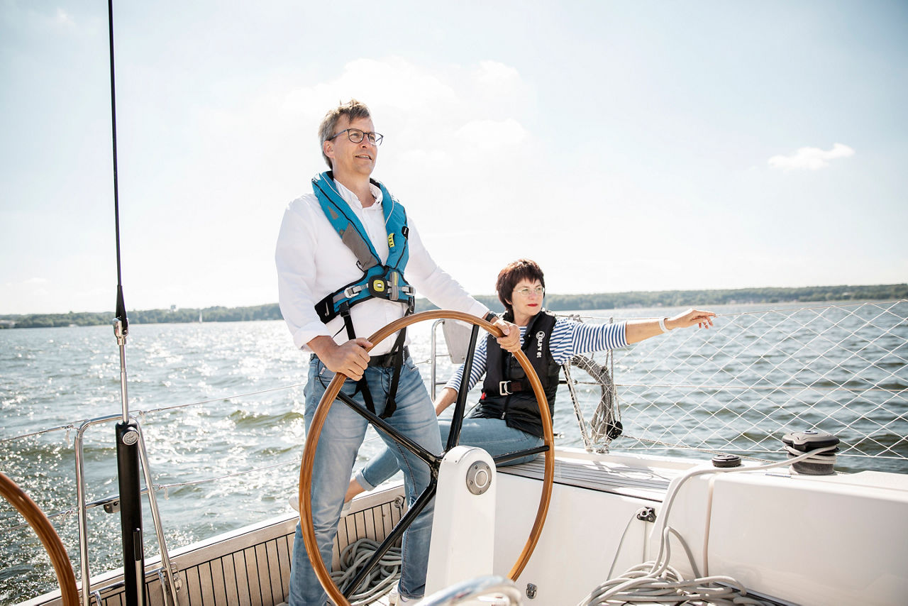 Ein Mann steuert das Segelboot, während eine Frau ihm den Kurs zeigt.