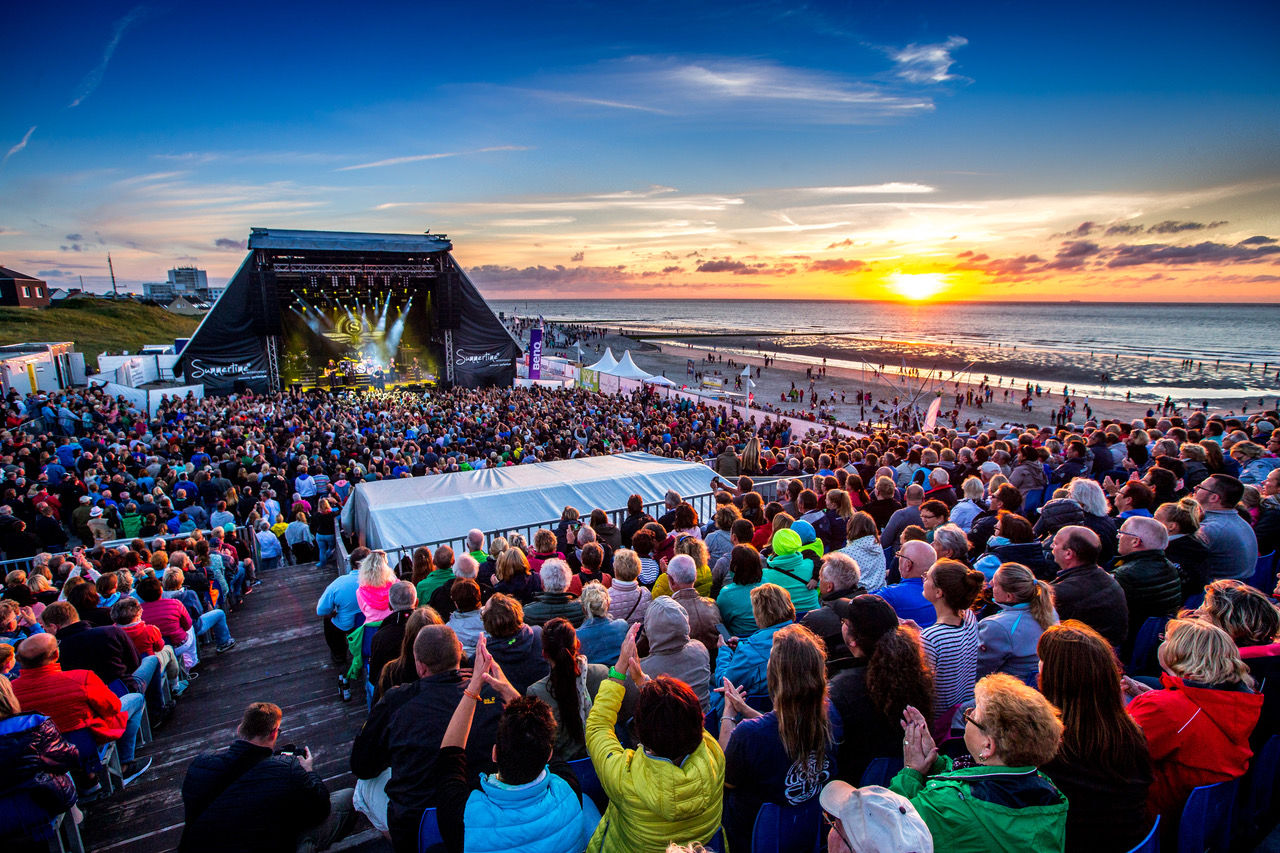 Menschen stehen im Sonnenuntergang vor der Bühne auf Norderney