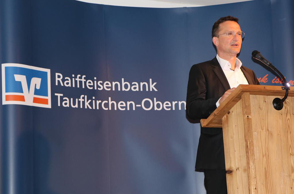 Ein Mann hält eine Rede auf einer Kanzel mit dem Logo der Bank im Hintergrund