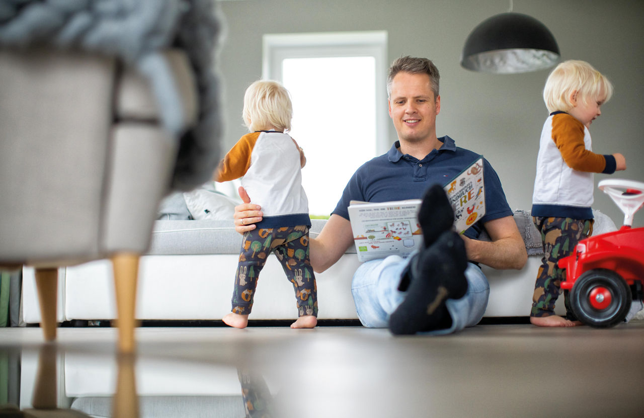 Vater sitzt lächelnd im Wohnzimmer mit seinen beiden Kindern
